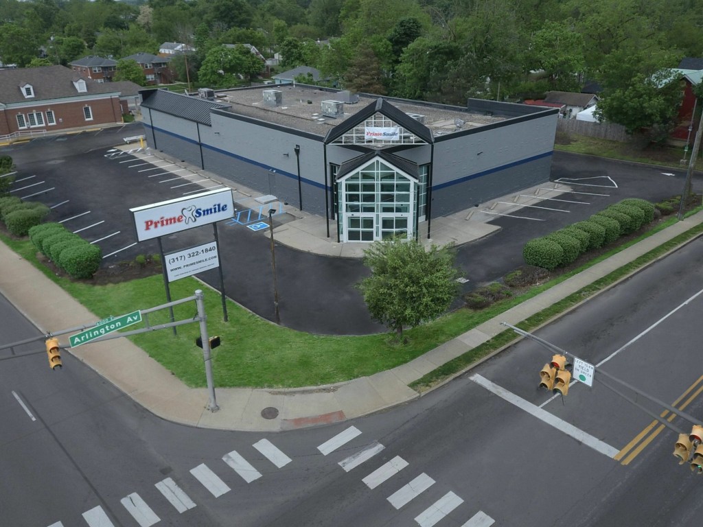 Aerial drone view of a Prime Smile dental building and parking lot located near a street intersection on Arlington Avenue