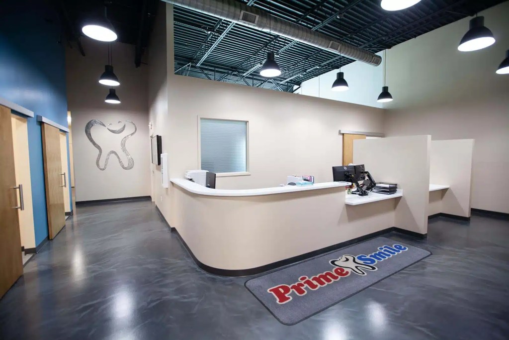 Curved front reception desk and check-in area of a Prime Smile clinic featuring a logo entrance floor mat