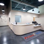 Curved front reception desk and check-in area of a Prime Smile clinic featuring a logo entrance floor mat