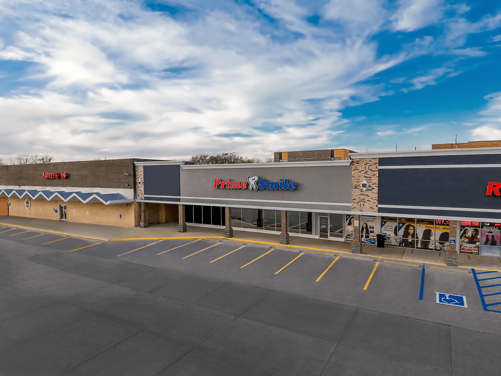 Exterior view of a retail shopping center building featuring a Prime Smile office sign and front parking spaces.